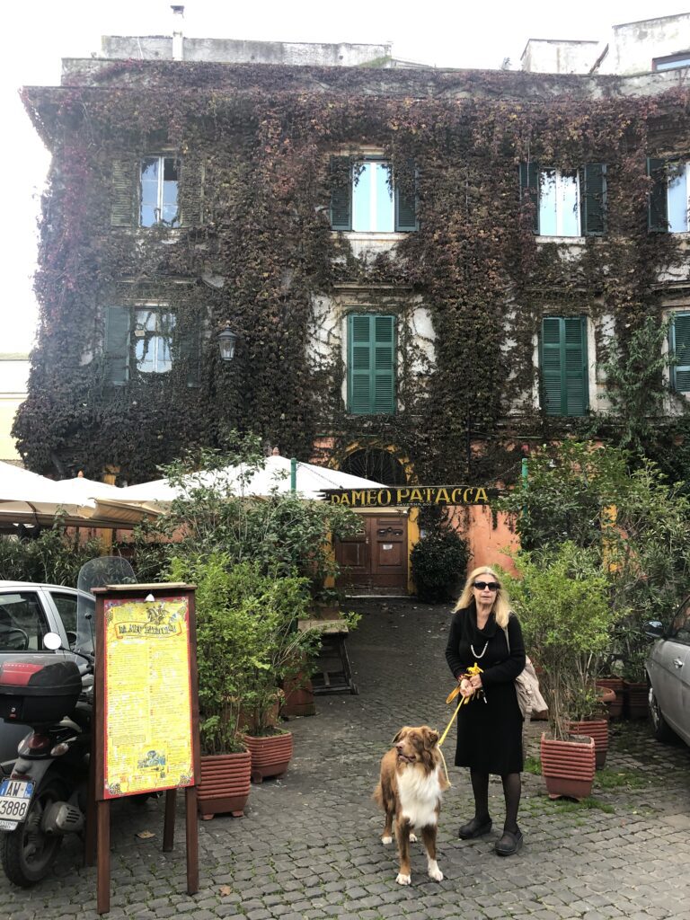a woman and her dog stand infront of a beautiful ivy-covered building in Italy